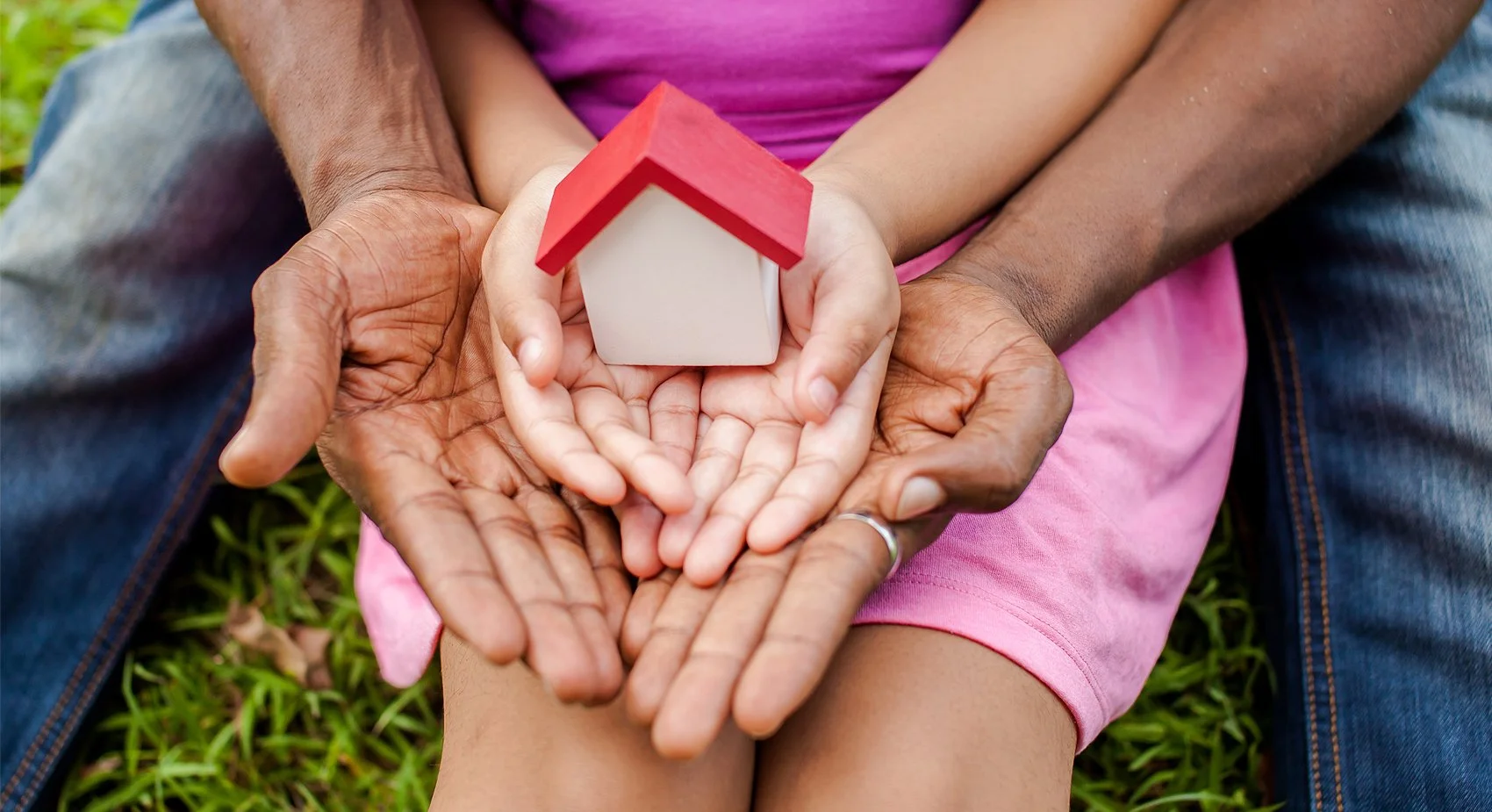 adult hands clasping child hands, which are then holding a small wooden toy house