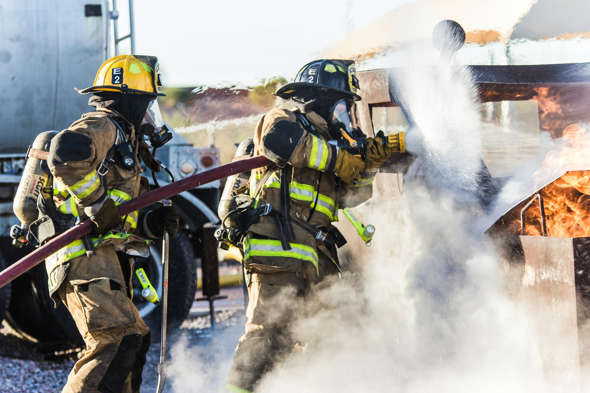 two firefighters working a hose on a fire outdoors