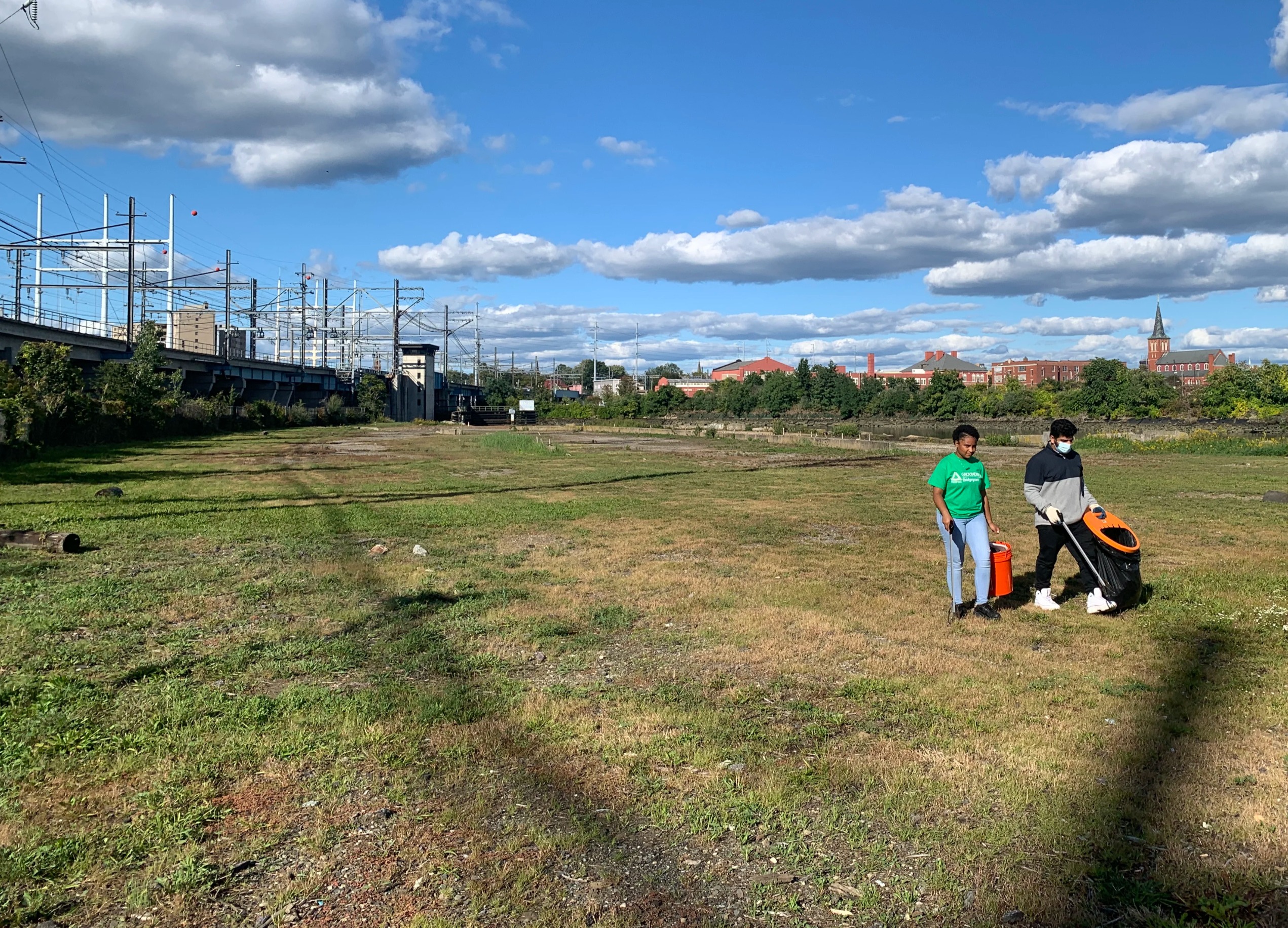 2 people walking across an empty lot and picking up trash