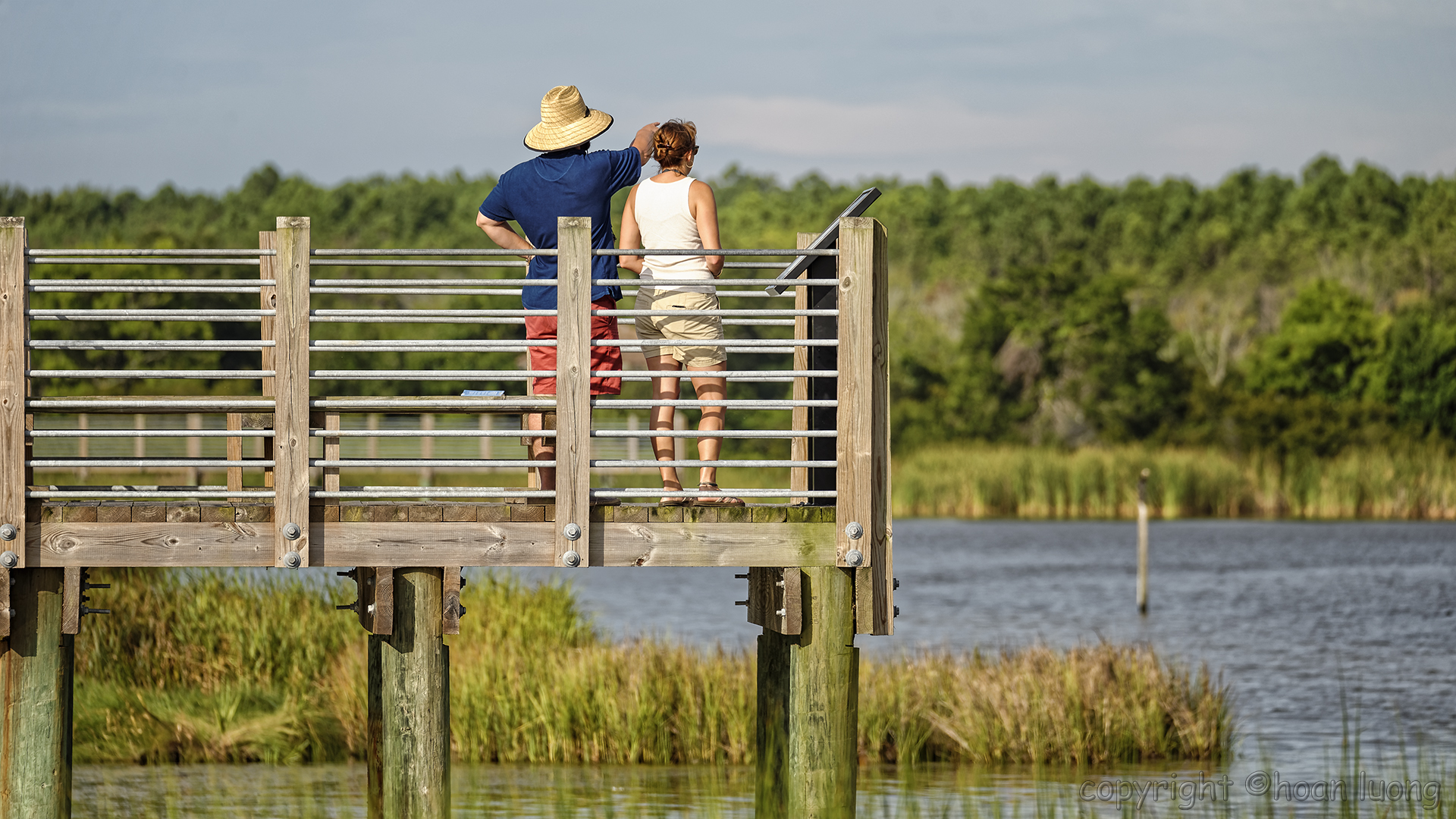 two people are standing at a river dock looking out into the water
